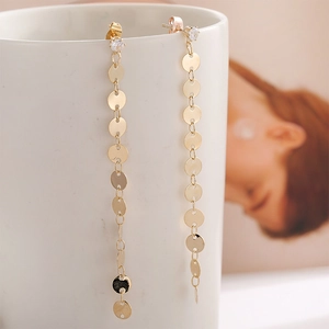 Close-up of golden long tassel earrings with small polished discs hanging on a white cup