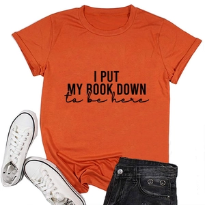 Flat lay of an orange cotton T-shirt with I Put My Book Down quote and casual accessories