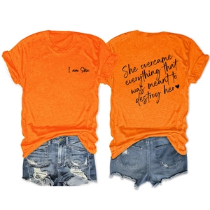 Detail view of orange cotton t-shirt with She Overcame Everything print and heart logo