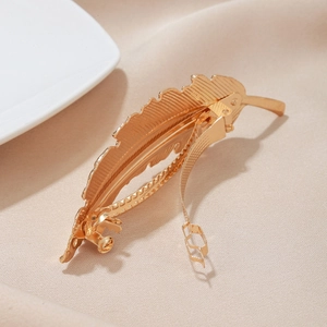 Elegant golden feather hair clip with vintage metal texture on neutral background