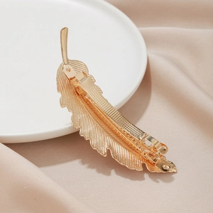 Elegant gold feather metal hair clip with detailed texture on champagne silk background