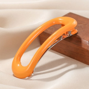 Bright orange oval acetate hair clip with silver spring metal fastener on wood display