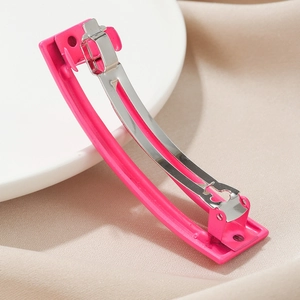 Detail view of pink acetate hair clip with silver spring mechanism on a white plate