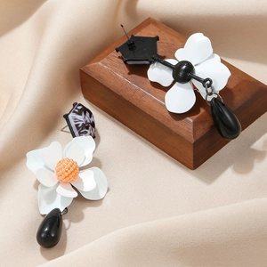 Detail of floral earrings featuring white petals, orange pistil, and black teardrop pendant