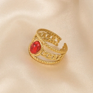 Detail of gold-plated stainless steel snake ring with red gemstone on silk background