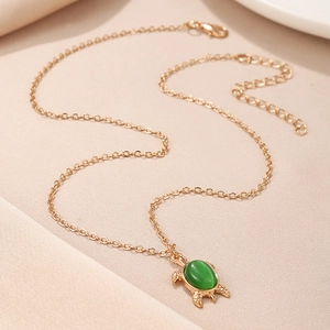 Detailed view of turtle pendant featuring a green oval stone on a gold necklace chain