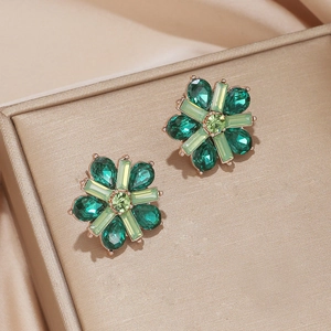Detail shot of flower-shaped earrings with green crystals on a gold base