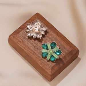 Detail view of green petal-shaped stud earrings with crystal stones on satin fabric