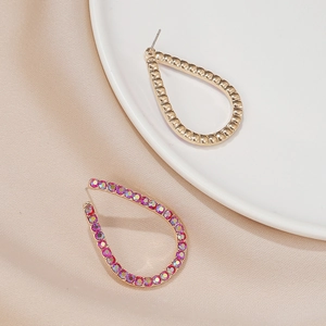Dettaglio di orecchini a goccia in oro martellato con cristalli rosa su seta beige