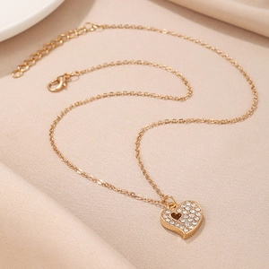 Close-up of a gold heart pendant necklace with pave crystal stones on beige leather
