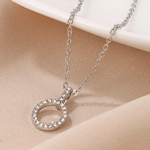 Close-up of a silver necklace with a hollow round pendant inlaid with white crystals