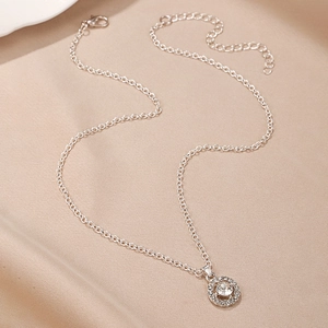 Detailed macro view of a silver-toned necklace with a sparkling crystal halo pendant on silk