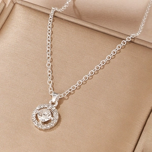 Macro shot of a silver necklace featuring a round pendant with a large crystal and pavé rhinestones