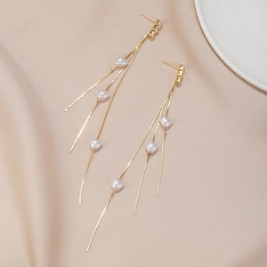 Vue détaillée de longues boucles d'oreilles pompons dorés et perles de cœur sur tissu