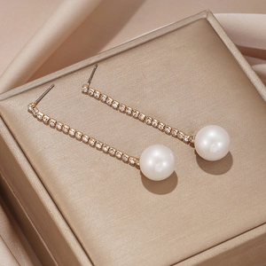 Vue macro de boucles d'oreilles perles avec chaînes dorées serties de diamants sur du satin