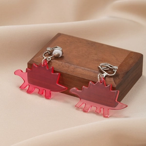 Macro detail of red translucent acrylic dinosaur ear clips on a dark wooden box