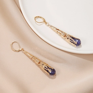 Detail van vintage gouden druppeloorbellen met paars kristal en opengewerkt metaal