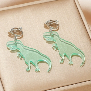 Close-up of cute light green acrylic dinosaur ear clips for girls on a gold texture box