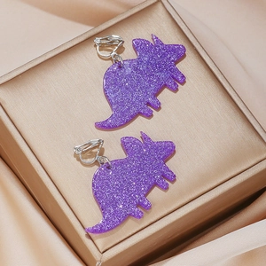Detail of purple glitter triceratops clip-on earrings for kids on luxury gold satin
