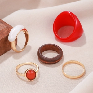 5-piece fashion ring set with red resin, gold metal and natural wood on beige fabric