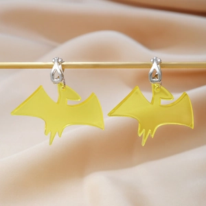 Macro view of translucent yellow pterosaur acrylic earrings hanging on a gold display stand