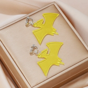 Detail of yellow acrylic bat clip-on earrings displayed on luxury silk and golden box