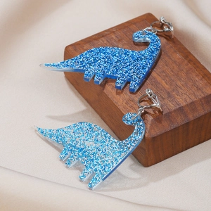 Detail of blue glitter acrylic dinosaur clip-on earrings on decorative background