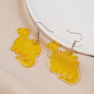 Close-up of yellow acrylic dinosaur earrings with silver hooks on a soft beige fabric