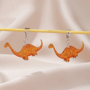 Detail of glitter orange acrylic dinosaur clip-on earrings for kids on silk fabric