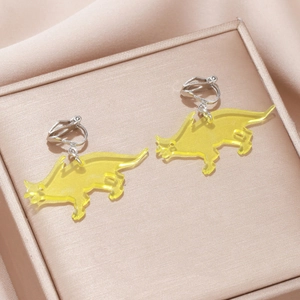 Detail view of yellow dinosaur acrylic clip-on earrings on a silk jewelry gift box