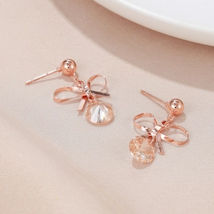 Detail of rose gold bow earrings with champagne crystals on a beige silk background