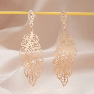 Exquisite hollow leaf gold tassel earrings hanging on display with pink satin backdrop