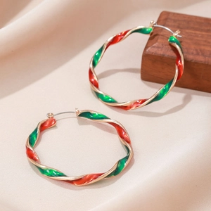 Detail of festive red and green enamel twisted hoop earrings on beige satin fabric