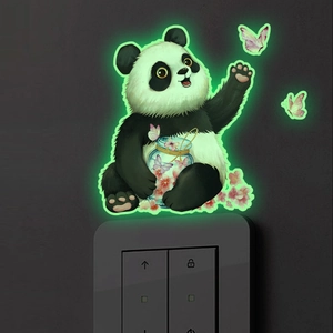 Luminous panda wall sticker glowing in green light on a dark wall switch panel
