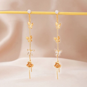 Macro detail of golden butterfly tassel earrings with sparkling zircon and rose pendant