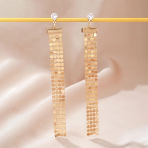 Macro detail of gold mesh fringe earrings featuring a round zircon stud on pink satin