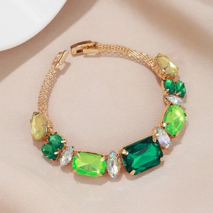 Détail d'un bracelet aux pierres précieuses vert émeraude et jaunes sur du satin