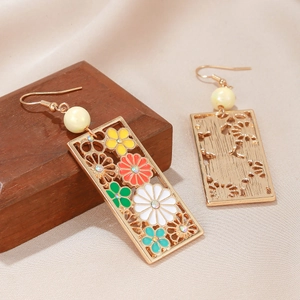 Eleganti orecchini a fiori traforati con smalto colorato e perle su fondo in legno caldo