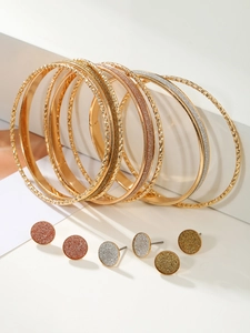 Detail of stacked metal bangles and glitter stud earrings in gold, silver, and rose gold