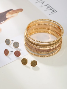 Detail of chunky gold bangle set and matte metallic stud earrings on a fashion magazine