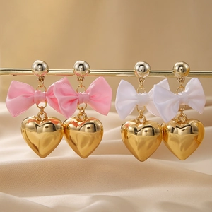 Boucles d'oreilles cœur doré avec nœuds en satin rose et blanc sur fond de soie champagne