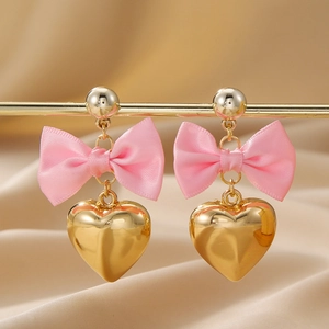 Détail de boucles d'oreilles cœur doré avec nœud en satin rose sur tissu champagne chic