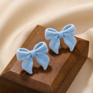 Détail de boucles d'oreilles nœud floqué bleu clair sur support bois et fond en soie satinée