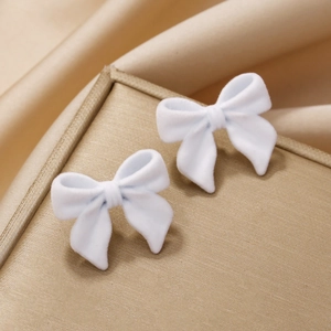 Boucles d'oreilles nœuds blancs floqués sur présentoir doré et fond en soie