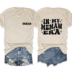 Flat lay of beige In My Memaw Era t-shirt with blue denim shorts showing front and back