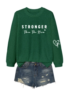 Close-up of STRONGER Than The Storm print on green sweatshirt and distressed denim shorts