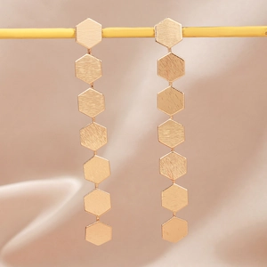 Minimalist matte gold hexagonal disc drop earrings displayed on elegant beige silk fabric