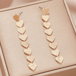 Close-up of gold brushed heart tassel earrings resting on a matching jewelry box