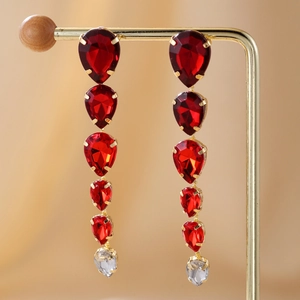 Detail of gold drop earrings with red pear-cut crystals on warm silk background
