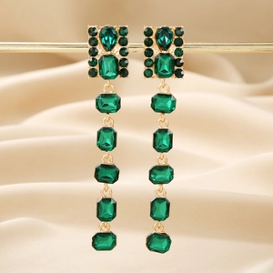 Macro view of long emerald green geometric earrings with gold dripping fringe on silk